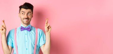 Umut dolu papyonlu yakışıklı adam, şans diliyor, şans diliyor ve sola bakıyor, sonuçları bekliyor ya da dua ediyor, pembe arka planda duruyor..