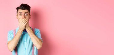 Şok olmuş ve nutku tutulmuş adam ağzını kapattı, elleriyle dudaklarını kapadı ve kameraya baktı, pembe arka planda duruyordu..