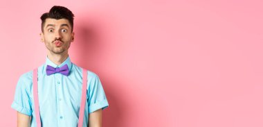 Öpüşmeyi bekleyen buruşuk dudaklı, aptal suratlı romantik pembe arka planda duran komik genç adam. Aşk ve Sevgililer Günü kavramı.