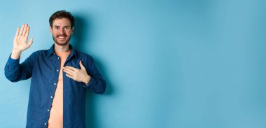 Mutlu genç adam kendini tanıtıyor. Elleri yüreğinde ve dostça gülümseyerek mavi arka planda durarak gerçeği söylüyor..