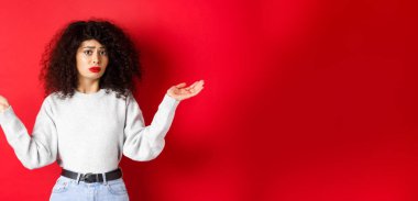 Kim bilir? Kıvırcık saçlı, omuz silkmiş, kafası karışmış, kırmızı arka planda sıradan kıyafetlerle duran cahil bir genç kadın..