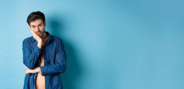 Üzgün ve sıkılmış bir adam elinde eğilmiş kameraya boş kafayla bakıyor, mavi arka planda sıkıntılı duruyor..