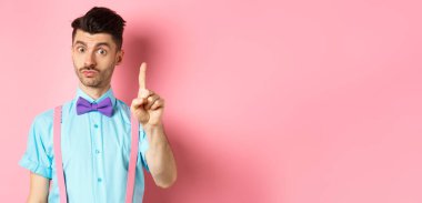 Genç, komik bir adam pembe arka planda duran bir şeyi açıklamak, seni yasaklamak ya da uyarmak için parmağını gösteriyor. Boşluğu kopyala