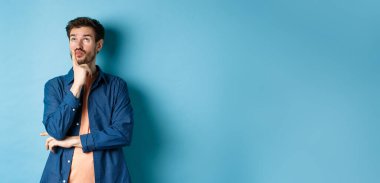 Düşünceli yakışıklı adam plan yapıyor, dalgın dalgın bakıyor, bir şeyler hayal ediyor, mavi arka planda duruyor..