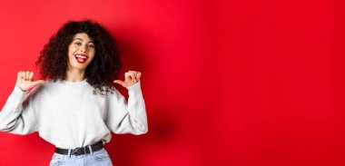 Kırmızı dudaklı, kendine güvenen, kendini beğenmiş, gösteriş meraklısı, kırmızı arka planda duran kendine güvenen genç bir kadın..