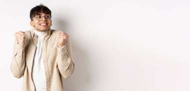 Yakışıklı, heyecanlı, motive olmuş ve şanslı bir adamın görüntüsü, sağa bakıyor ve gülümsüyor, zaferi kutlamak için yumruk hareketi yapıyor, ödülü kazanıyor, beyaz arka planda duruyor..