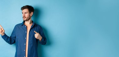 Kafkasyalı genç bir adamın görüntüsü, bir kenara bakıyor, reklamını yapıyor, mavi arka planda duruyor..