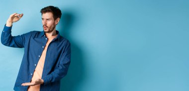 Büyük bir nesneyle boş alana bakan, büyük boyutlarda, mavi arka planda duran, etkileyici bir beyaz adam..