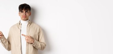 Gözlüklü, solu işaret eden, canı sıkkın, kötü tekliften şikayet eden, beyaz arka planda üzgün duran, hayal kırıklığına uğramış bir adam..