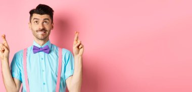 Papyonlu gülümseyen genç adam, dua ediyor, dua ediyor ve bakıyor, şans diliyor, pembe arka planda umutla bekliyor. Boşluğu kopyala