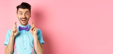 Mutlu adam dilek diliyor, şans dilemek için dua ediyor kameraya gülümsüyor, iyi haberi bekliyor, pembe arka planda duruyor..