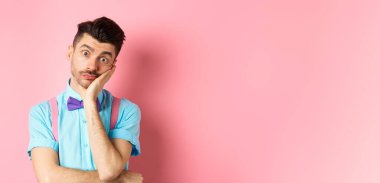 Shocked and tired caucasian guy staring pissed-off at camera, lean on palm and looking at something with skeptical face, standing over pink background.