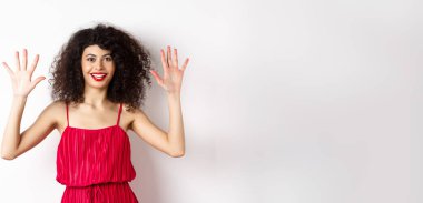 Kıvırcık saçlı, kırmızı elbiseli, on numarayı parmaklarıyla gösteren, beyaz arka planda duran güzel bir manken..