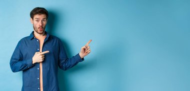 Şaşkın genç adam tanıtımı kontrol ediyor, parmaklarını logoya doğrultuyor ve 