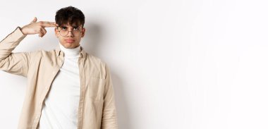 Sinirli genç adam kafasına silah hareketi yapıyor. Sıkıntıdan ya da sıkıntıdan kendini vuruyor. Beyaz arka planda duran aptalca bir şeyden bıkmış..