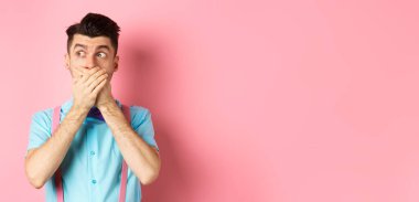 Şok olmuş adam çenesini kapattı, ellerle dudaklarını kapadı ve soluna baktı. Pembe arka planda şaşkınlık içinde durdu..