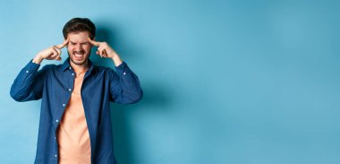 Hasta hisseden, başıyla temas eden, baş ağrısı çeken, baş dönmesi hisseden, mavi arka planda duran bir adam..