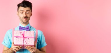 Tatiller ve kutlama konsepti. Mutlu gülümseyen adam sevgilisinden beyaz bir gün hediyesi alıyor. İlgi çekici bir yüz ifadesiyle pembe arka planda duruyor..