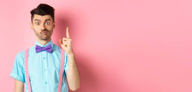 Eureka tabelasında parmağını kaldıran düşünceli bir adam sevgililer günü için hediye önerileri sunuyor, pembe arka planda duruyor..