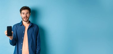 Mutlu beyaz adam boş bir ekran gösteriyor ve gülümsüyor, mavi arka planda duruyor..