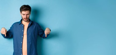 Modern bir adamın gündelik giysiler içinde boş alana bakıp işaret etmesi logo okuması, mavi arka planda durması..