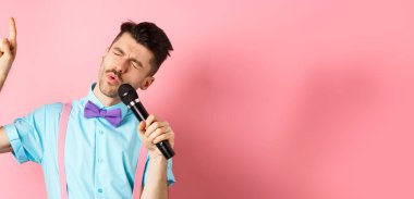 Parti ve festival konsepti. Komik adam mikrofonda şarkı söylüyor, parmağını kaldırıyor şarkıda yüksek notaya ulaşıyor, pembe arka planda duruyor..