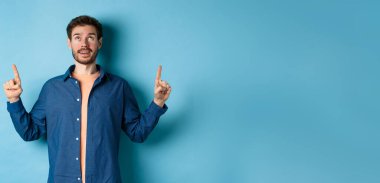 Heyecanlı Kafkasyalı adam işaret ediyor, reklamını yapıyor, mavi arka planda duruyor..