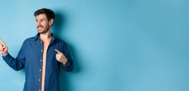 Gülümseyen yakışıklı adam boşluğu işaret edip sola bakıyor, logoyu gösteriyor, mavi arka planda duruyor..