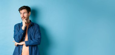 Düşünceli beyaz adam boş alana bakıyor ve düşünüyor, mavi arka planda dalgın dalgın duruyor. Boşluğu kopyala