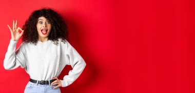 Heyecanlı güzel bir kadın evet diyor, iyi bir jest yapıyor ve hevesli görünüyor. Katılıyorum. İltifat ediyor, kırmızı arka planda duruyor..