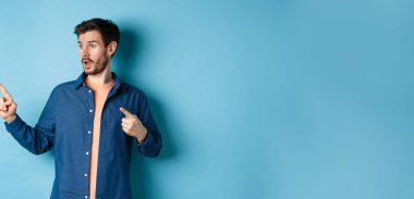 Gündelik giysiler içinde, boş alana bakıp duran, reklamını yapan, mavi arka planda duran, şaşırmış bir adam..