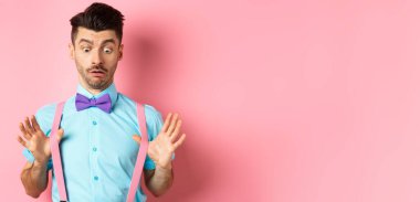 Bıyıklı ve papyonlu komik bir adam. Pantolon askılarını düzeltiyor ve şaşkın ve şaşkın bir suratla pembe arka planda dikiliyor..