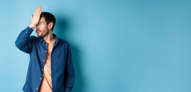 Sinirli ve yorgun adam facepalm, gözlerini devirme ve mavi arka planda duran aptal davranışlardan rahatsız olmuş görünme..