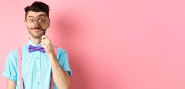 Bıyıklı, papyonlu, kocaman gözleriyle büyüteçten bakıp gülümseyen, pembe arka planda duran komik beyaz adam..