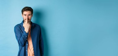 Ignorant and rude guy showing middle finger and smiling, say fuck you, standing on blue background.