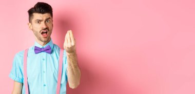 Düşüncesizce hareket eden genç bir adam, birinin hatalı olduğunu kanıtla, İtalyan jesti ve şikayeti göster, pembe arka planda dur..