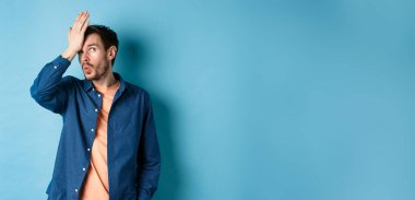 Sinirli bir adam aptal bir şeyden facepalm yapıyor ve gözlerini deviriyor. Mavi arka planda duruyor. Alnında bir el var..