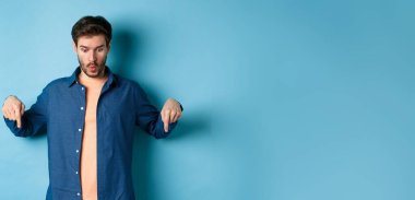 Günlük giysiler içinde etkileyici beyaz erkek manken, diyelim ki, vay canına, logoya bakıyor ve parmaklarıyla işaret ediyor, kırmızı arka planda duruyor..