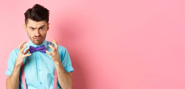 Image of angry guy in bow-tie gonna strangle someone, raising hands up and looking mad or pissed-off, feeling furious, standing on pink background.