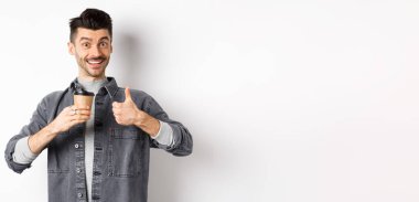 Çok iyi bir içki. Gülümseyen stil sahibi, kahve içen, başparmağını kaldıran, kahveciye övgüler yağdıran, beyaz arka planda duran.