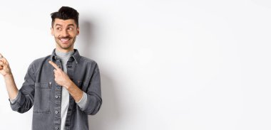 Mutlu yakışıklı adam gülümsüyor ve solu işaret ediyor, havalı ürünler gösteriyor, beyaz arka planda duruyor..