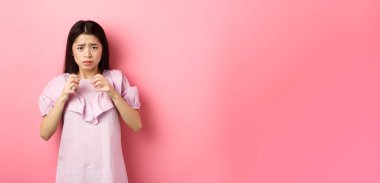 Korkak Asyalı kadın kurban, korkmuş görünüyor, korkudan titriyor, korkunç şeye bakıyor, pembe arka planda endişeli duruyor..