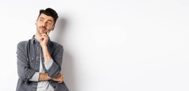 Düşünceli yakışıklı adam dalgın dalgın bakıyor, seçim yapıyor, beyaz arka planda duruyor..