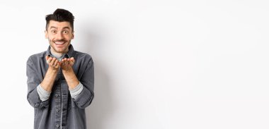 Tatlı genç adam kameraya hava öpücüğü yolluyor ve gülümsüyor. Umutsuz romantik aşkını gösteriyor, elinde bir şey tutuyor, beyaz arka planda duruyor..