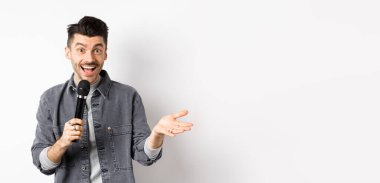 Mikrofonla konuşan, el kol hareketi yapan, mikrofonla konuşma yapan, beyaz arka planda duran yakışıklı bir sanatçı..