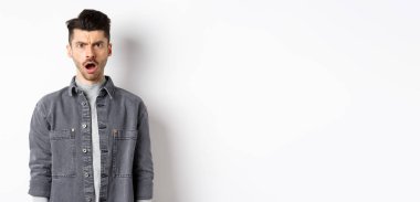 Şok olmuş ve gücenmiş bir adam, kameraya açık ağızla bakıyor, acımasız sözlerle incinmiş, beyaz arka planda hayal kırıklığına uğramış..