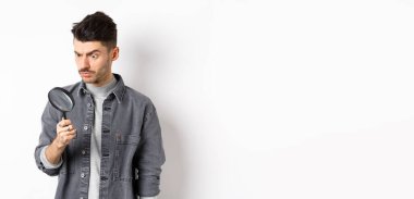 Ciddi araştırmacı, büyüteçle aşağı bakan, ciddi bakan, beyaz arka planda duran.