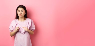 Korkak Asyalı genç kız yumruklarını sıkmış ve kameraya bakıyor. Pembe arka planda duran korkunç bir şeyden korkuyor..