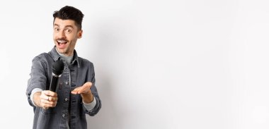 Yakışıklı gülümseyen adam mikrofonla elini uzatıyor, mikrofonu sana veriyor, beyaz arka planda duruyor..