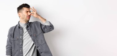 İğrenç adam arkasını döndü ve burnunu kötü kokuya kapattı. İğrenç kokuyordu, beyaz arka planda duruyordu..